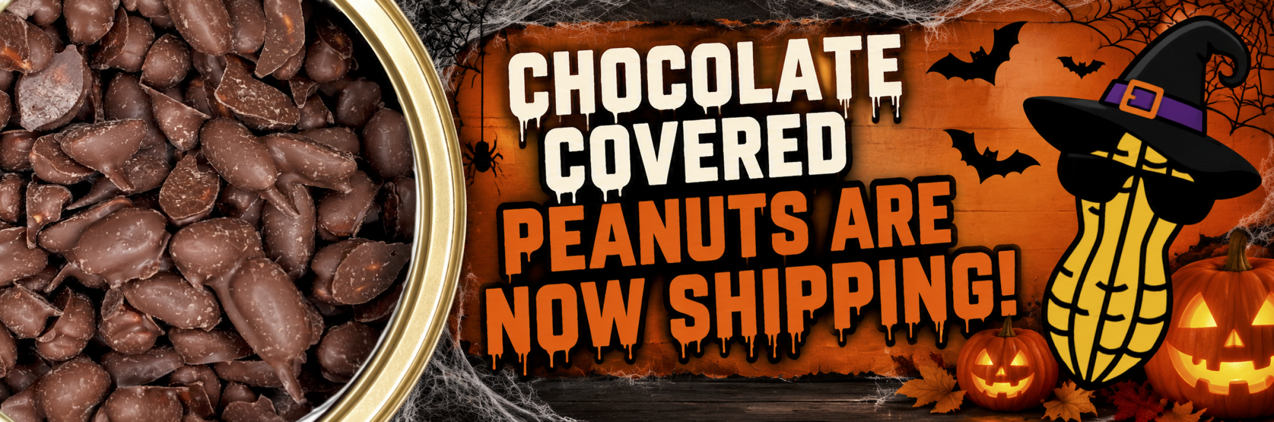 A tin of halloween candy chocolate covered peanuts hancock peanuts next to a Halloween-themed sign that reads Chocolate covered peanuts are now shipping! featuring a cartoon peanut in a witch’s hat and sunglasses, amidst bats and jack-o-lanterns.